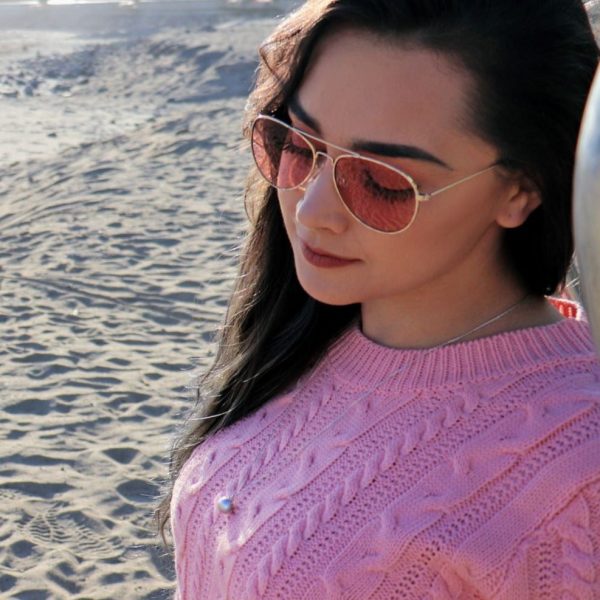 brunette woman on beach in pink sweater and sunglasses wearing gray pearl necklace pendant