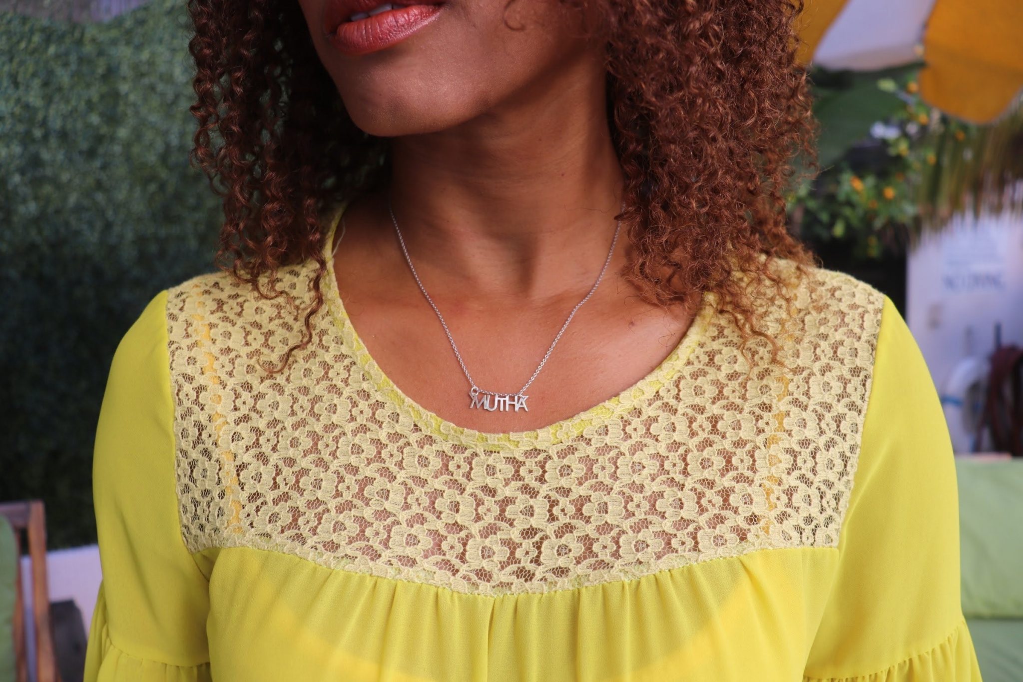 black woman with curly hair in a yellow dress wearing a silver Mutha necklace from the wandering jewel