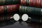 Silver lady Justice cufflinks from the wandering jewel set on a table in front of a bunch of books