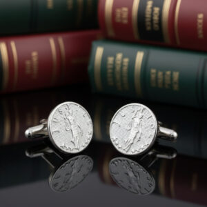 Silver lady Justice cufflinks from the wandering jewel set on a table in front of a bunch of books