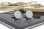 silver power button Cufflinks from the wandering jewel sitting on top of a black reflective ipad