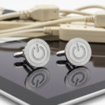 silver power button Cufflinks from the wandering jewel sitting on top of a black reflective ipad