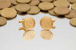 gold landline symbol cufflinks from the wandering jewel with phones on the face sitting on top of a mirrored surface with gold coins in the background