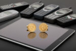 gold landline phone symbol cufflinks from the wandering jewel with phones on the face sitting on top of an iPad with black retro cell phones in the background