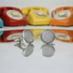 silver cufflinks with a receiver phone landline symbol from the wandering jewel on the face reflecting on a mirror with colorful retro rotary phones in the background